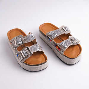 Silver embellished sandals with brown soles on a white background