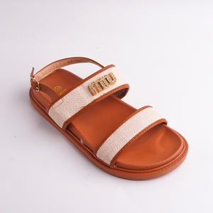 Brown sandal with beige strap and gold logo on a light gray background