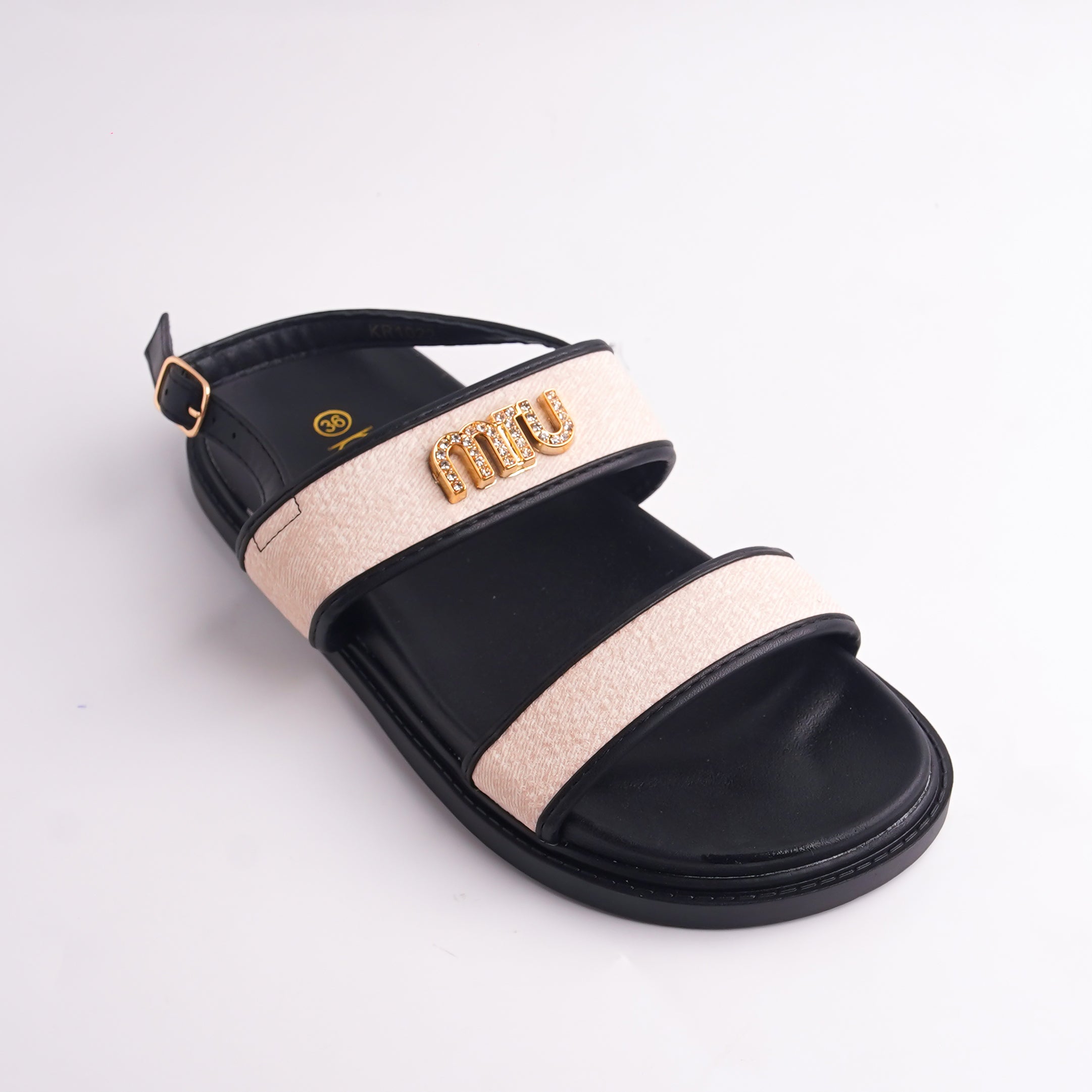 Black sandal with beige strap and gold logo on a light gray background