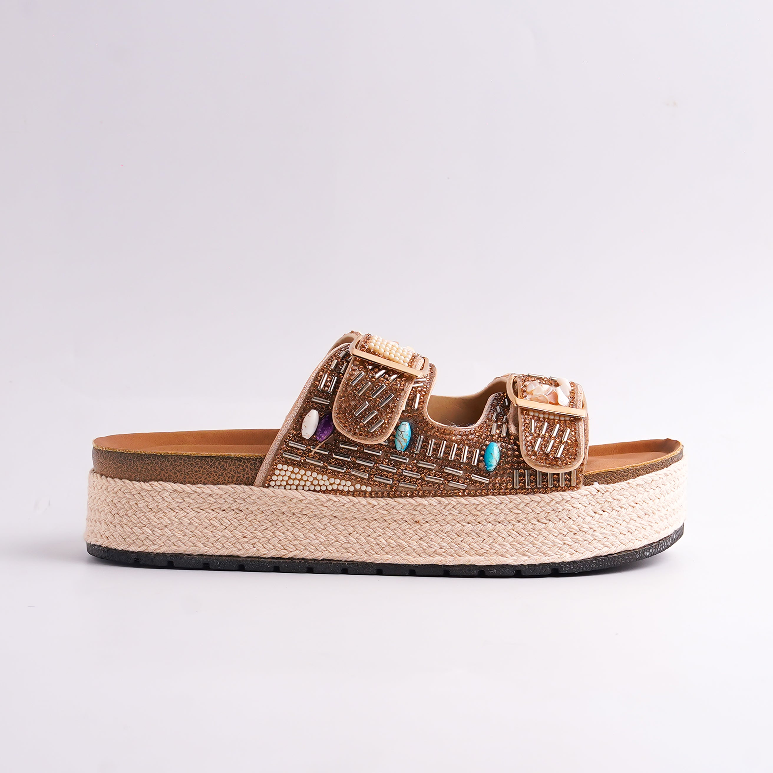 Beige sandal with decorative straps and turquoise stones on a light gray background