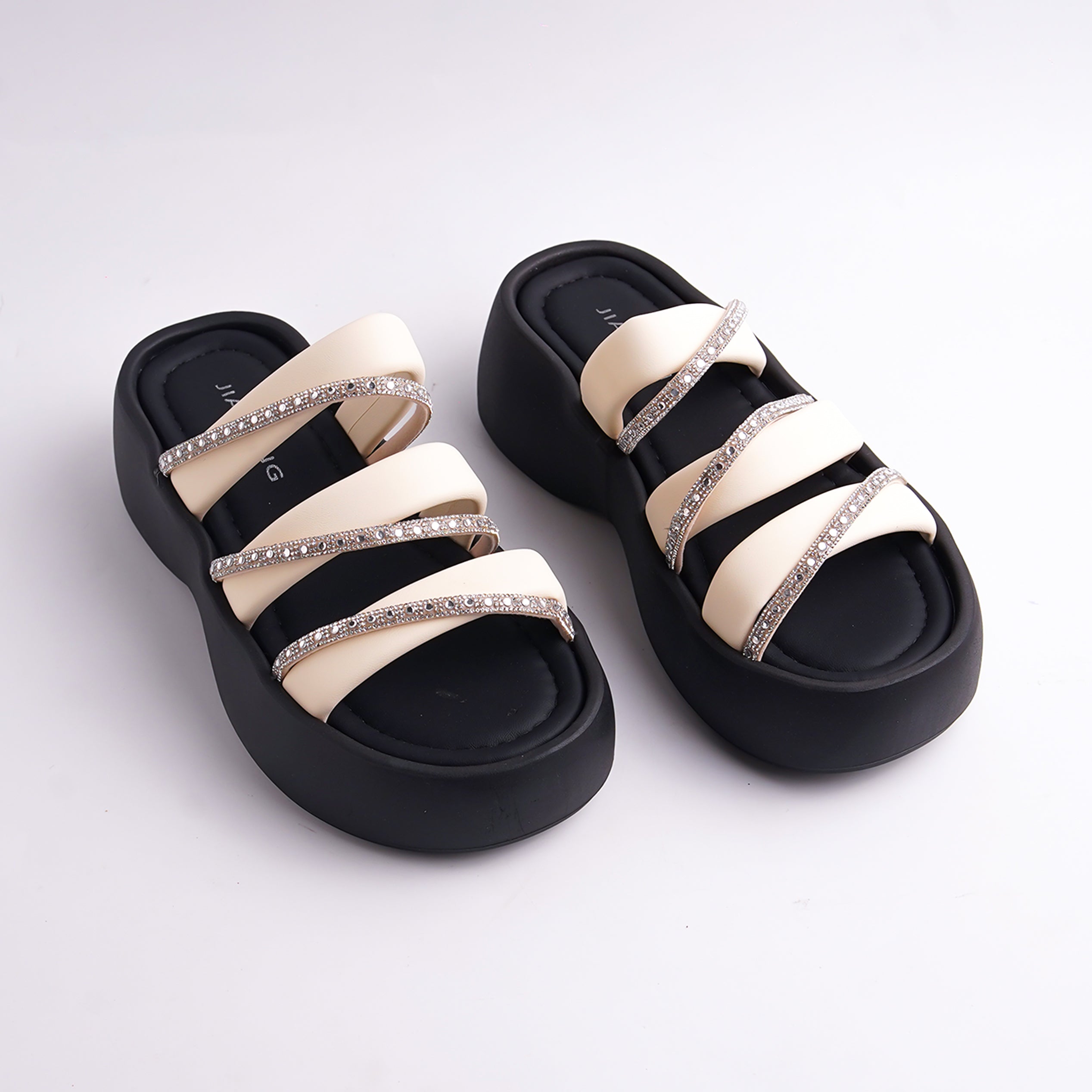 Pair of black and beige sandals with rhinestone straps on a white background