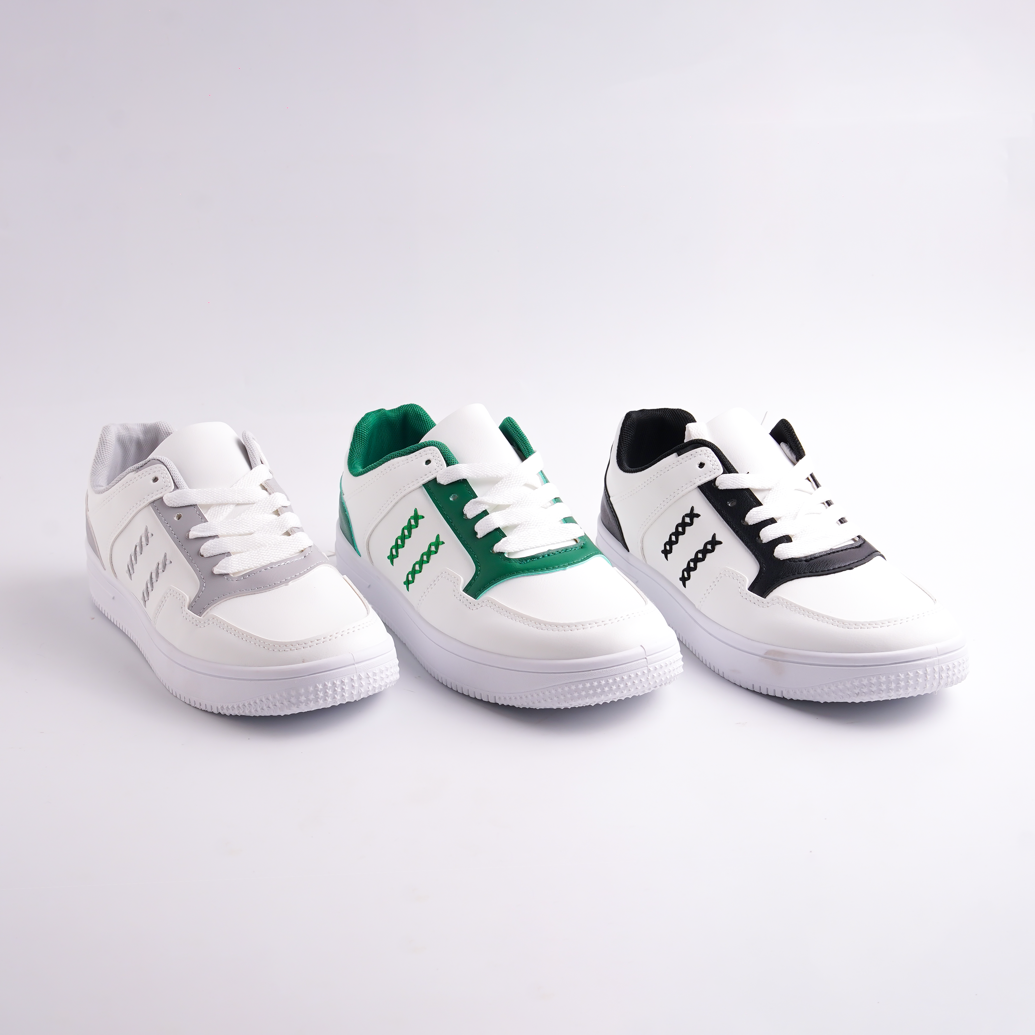 Three white sneakers with green and black accents on a light gray background